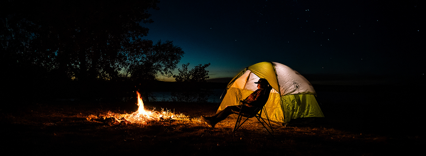 A woman sitting under a sky of stars in front of a tent and campfire in Platte County, Wyoming